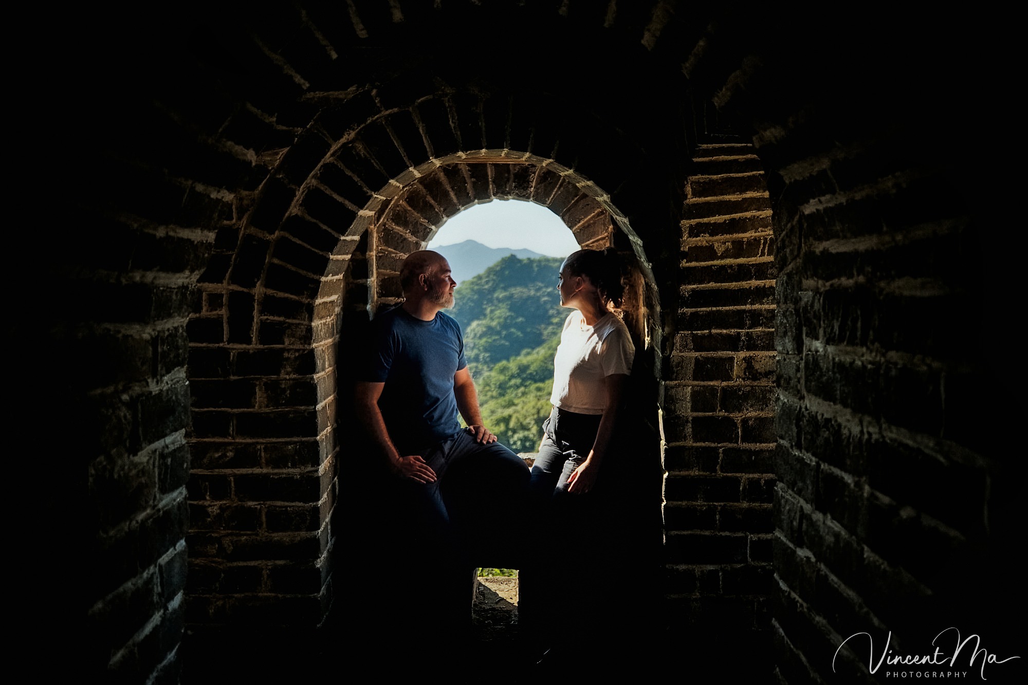 An American couple posing for romantic pictures against the backdrop of Mutianyu Great Wall in Beijing, China. The Great Wall winds through the mountains, and the couple shows their love in the photos