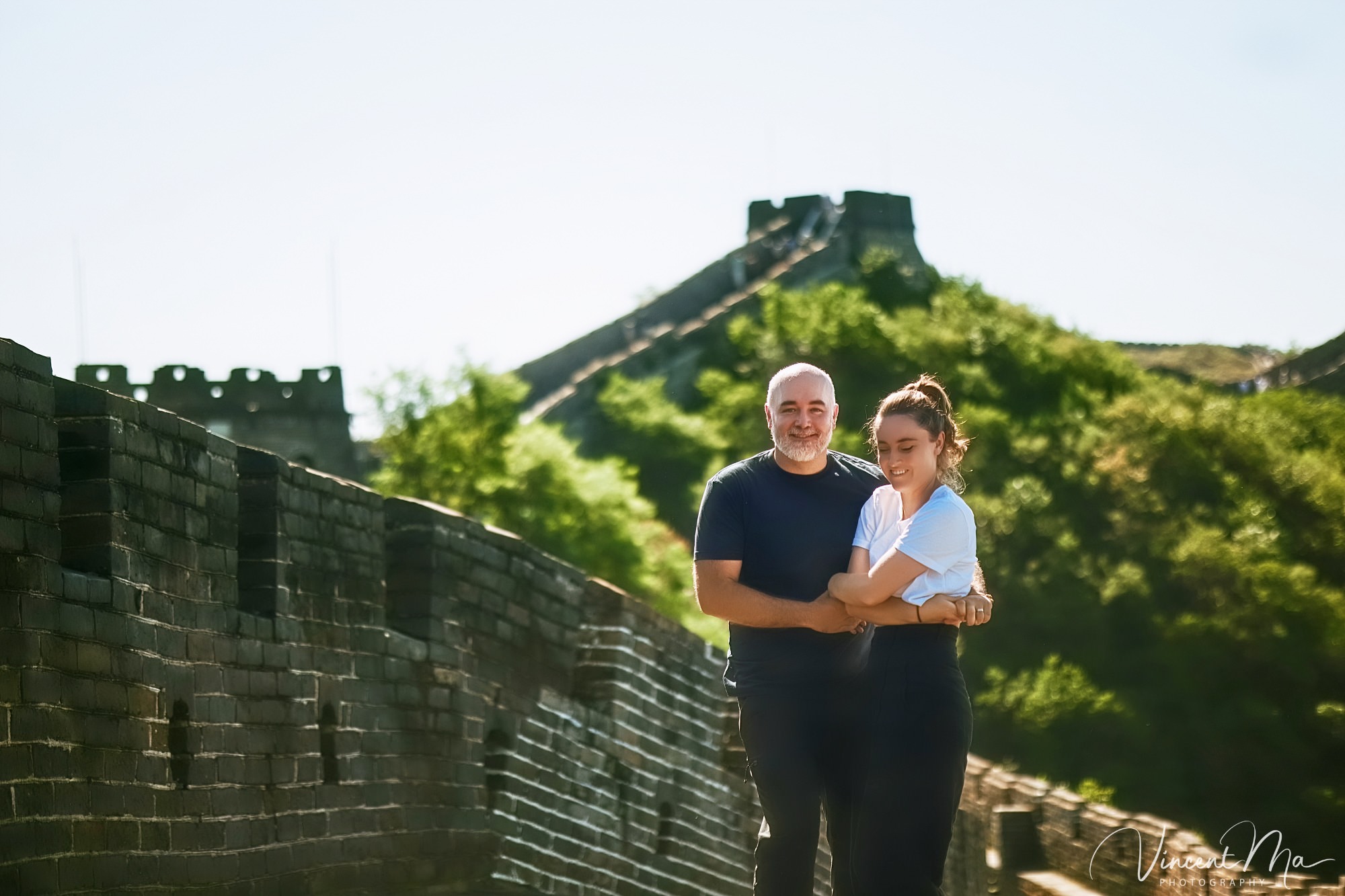 An American couple posing for romantic pictures against the backdrop of Mutianyu Great Wall in Beijing, China. The Great Wall winds through the mountains, and the couple shows their love in the photos