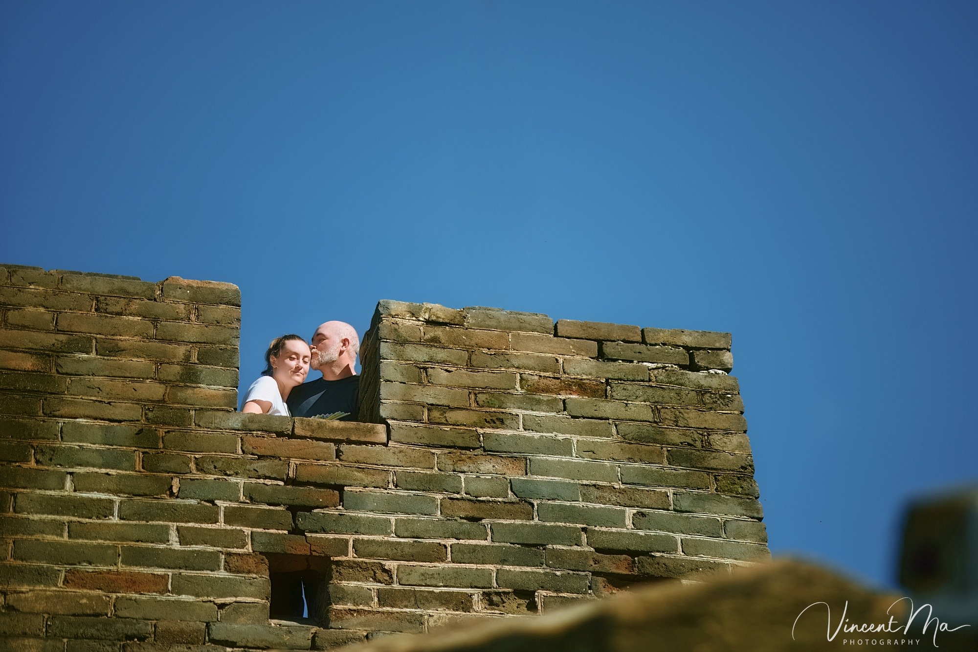 An American couple posing for romantic pictures against the backdrop of Mutianyu Great Wall in Beijing, China. The Great Wall winds through the mountains, and the couple shows their love in the photos