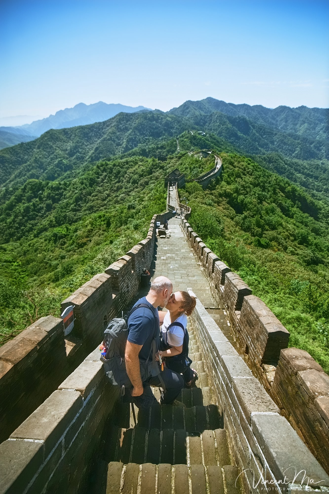An American couple posing for romantic pictures against the backdrop of Mutianyu Great Wall in Beijing, China. The Great Wall winds through the mountains, and the couple shows their love in the photos