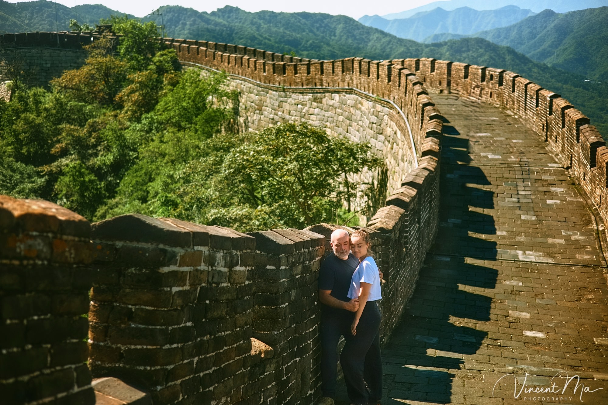 An American couple posing for romantic pictures against the backdrop of Mutianyu Great Wall in Beijing, China. The Great Wall winds through the mountains, and the couple shows their love in the photos