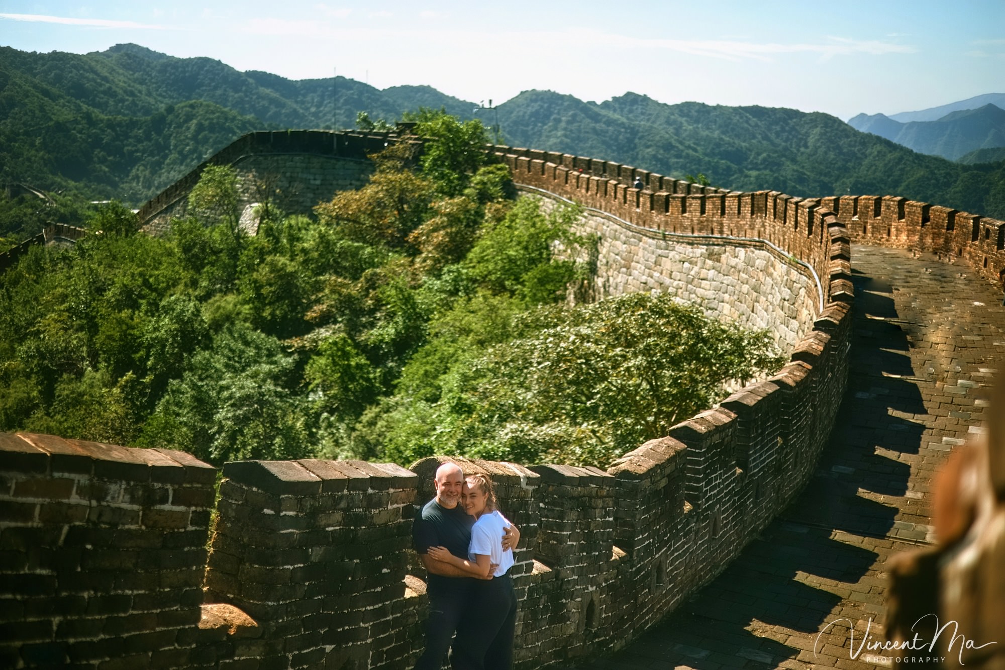 An American couple posing for romantic pictures against the backdrop of Mutianyu Great Wall in Beijing, China. The Great Wall winds through the mountains, and the couple shows their love in the photos