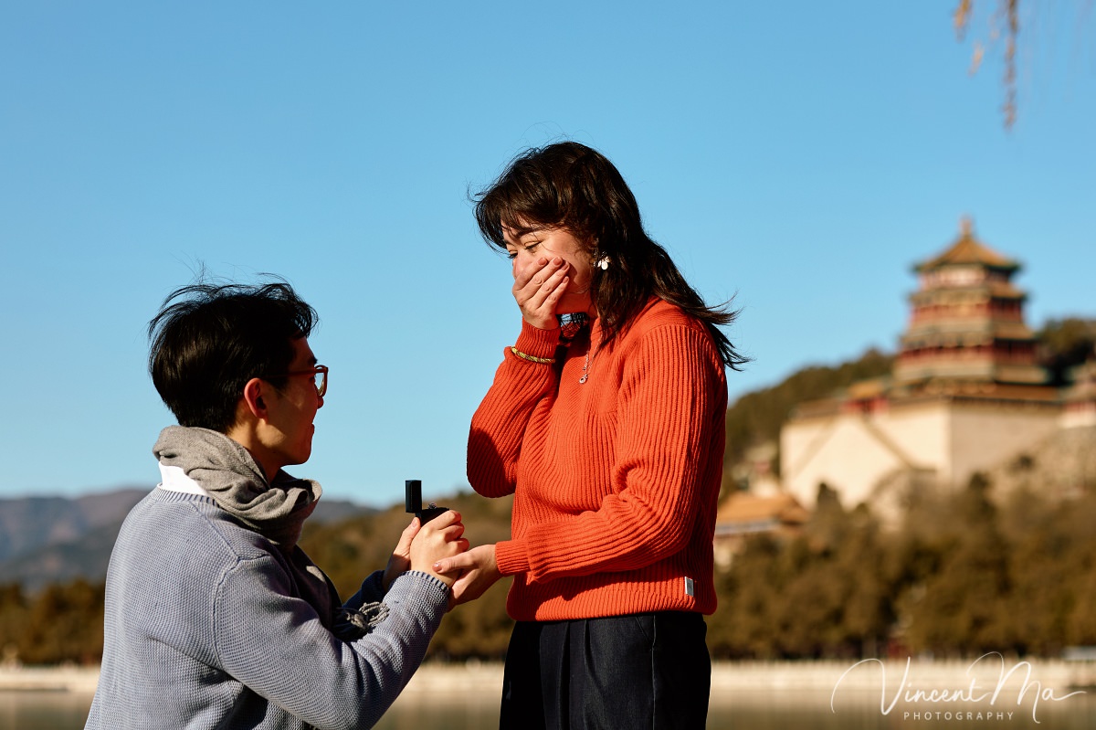 Beijing proposal.Couple sharing a romantic kiss with the Tower of Buddhist Incense in the background at the Summer Palace, Beijing. Winter engagement photography with clear blue sky