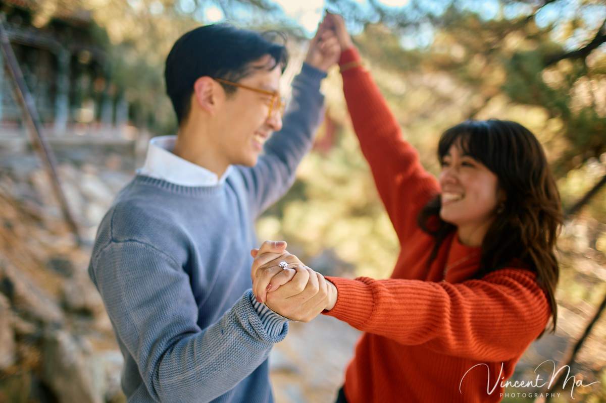 Beijing engagement photography. Couple looking at each other lovingly on a stone bridge at the Summer Palace. Traditional Chinese pavilion and winter reeds in the background.