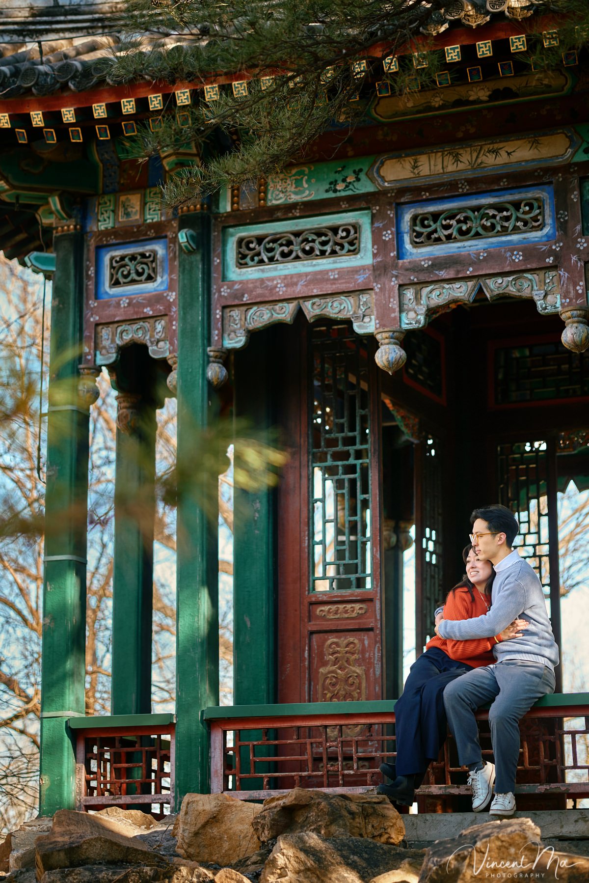Beijing engagement photography. Couple looking at each other lovingly on a stone bridge at the Summer Palace. Traditional Chinese pavilion and winter reeds in the background.