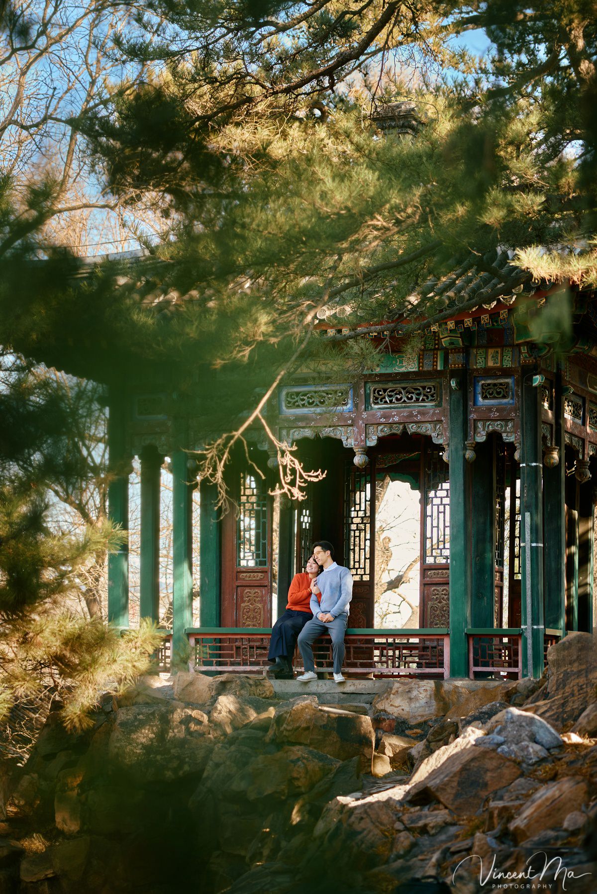 Beijing engagement photography. Couple looking at each other lovingly on a stone bridge at the Summer Palace. Traditional Chinese pavilion and winter reeds in the background.
