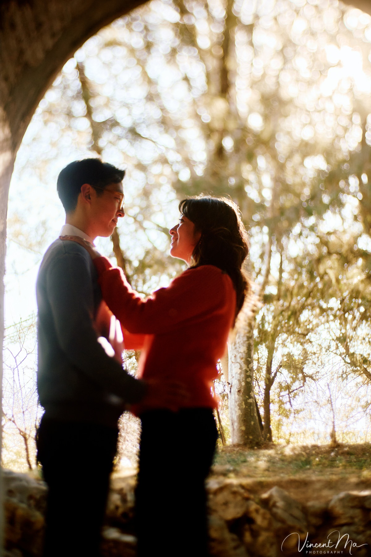 Beijing engagement photography. Couple looking at each other lovingly on a stone bridge at the Summer Palace. Traditional Chinese pavilion and winter reeds in the background.